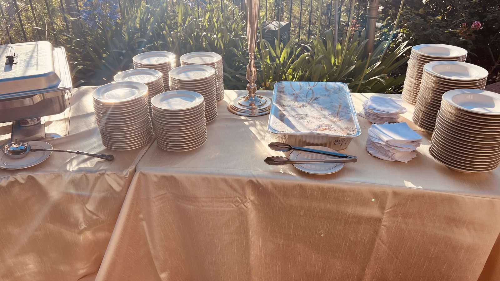 Chafing dishes and stacked plates set for a Honest catering buffet at golden hour